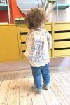 Child with curly hair turned around and holding a Herr Menig Junior tote bag in front of a yellow retail display