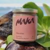 a hand coming out the side of the frame holding a hawaiian macadamia nut butter jar with a gold top and the maka logo and packaging design in front of an island landscape suggesting hawaiian beaches