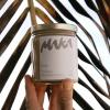 artistic photo of a hand coming out the bottom of the frame holding a hawaiian macadamia nut butter jar with a gold top and the maka logo and packaging design in front of an abstract, zoomed in background of a palm leaf